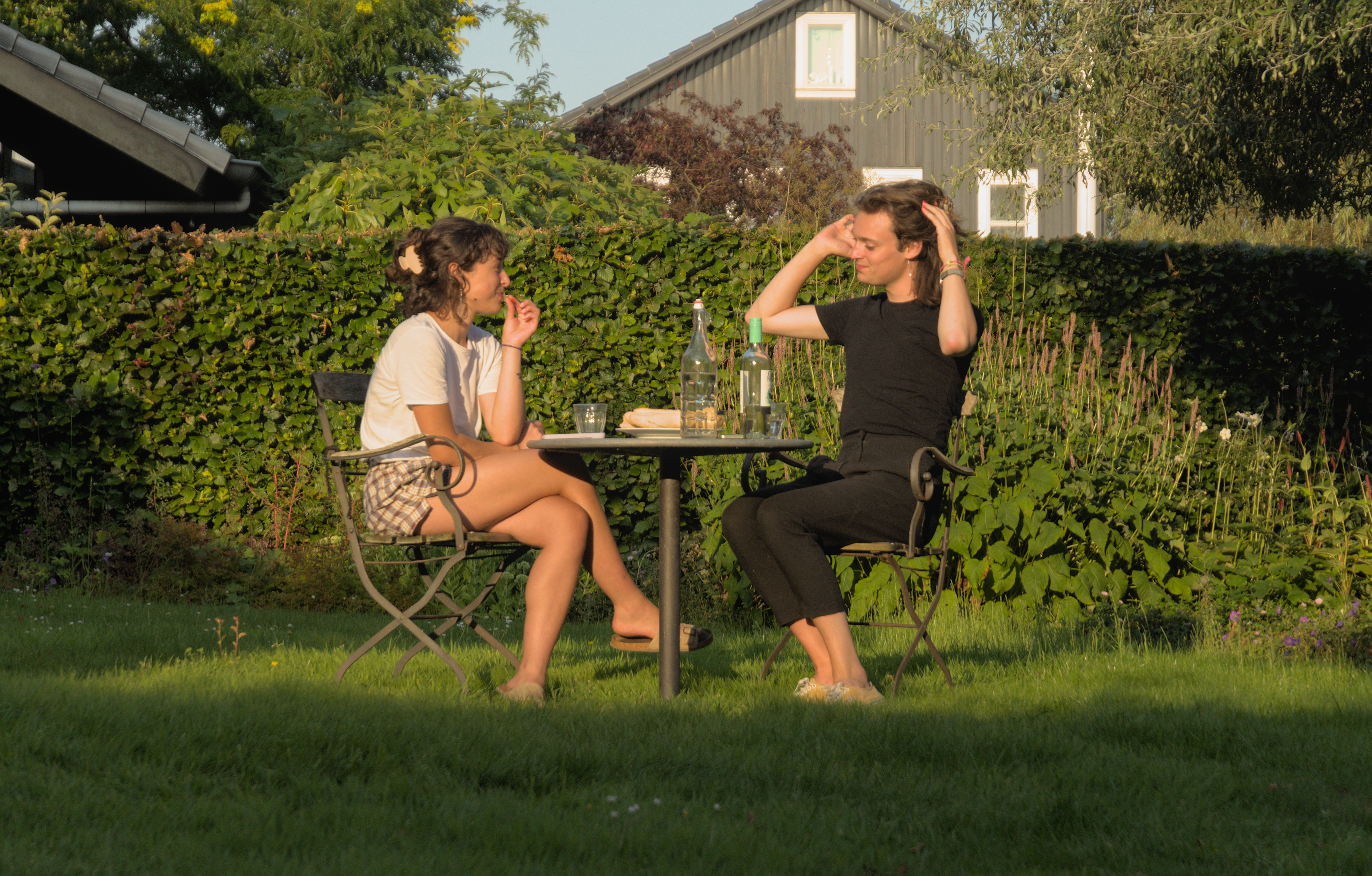 We sit right in the middle of a lawn around a small round table on bistro-style chairs. The sun hits us and everything behind us, while the foreground is cast in shadow as the sun is setting.

